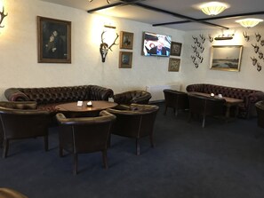 Cómoda sala de estar con sofás y sillones de cuero, un televisor montado en la pared y diversas imágenes y cuernos decorando las paredes.