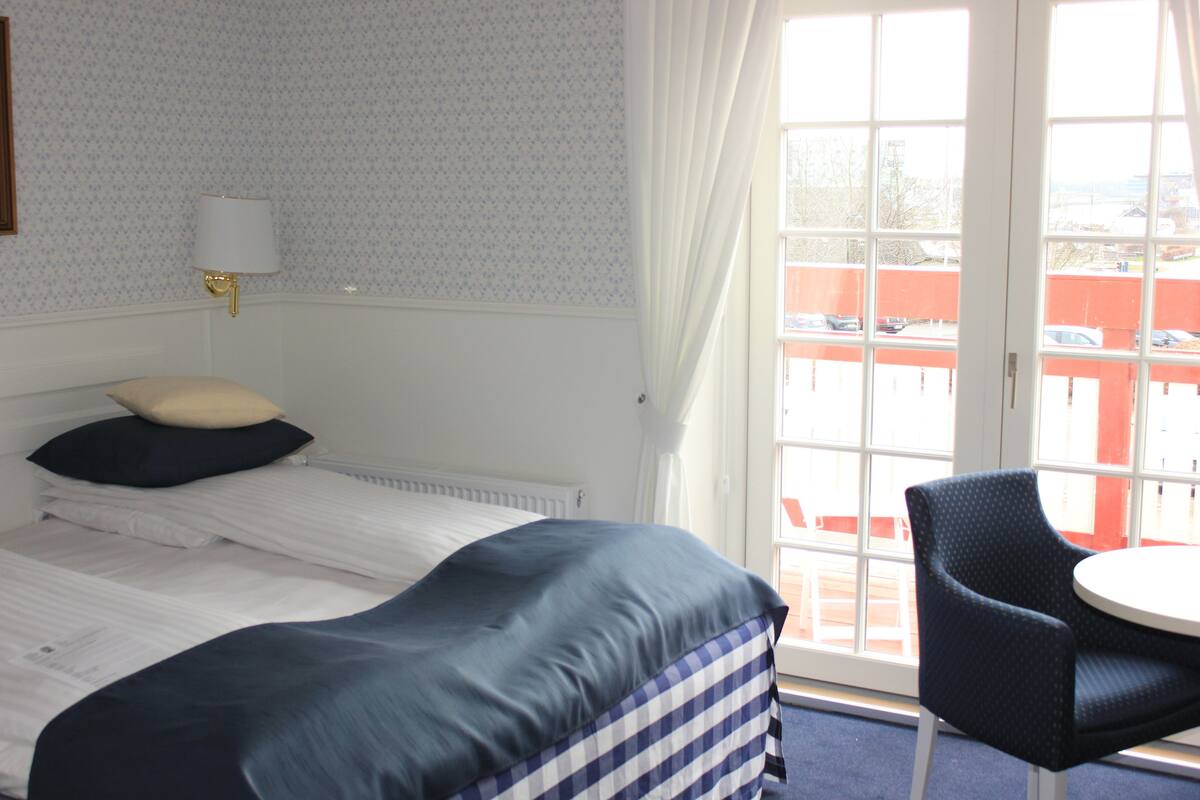 Una habitación de hotel con cama, una silla, una ventana con cortinas y un papel tapiz estampado en la pared.