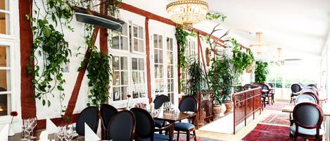 Un restaurante con mesas y sillas de madera y plantas colgantes.