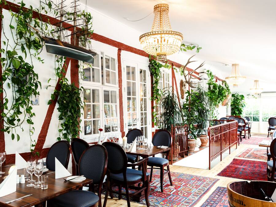 Un restaurante con mesas y sillas de madera y plantas colgantes.