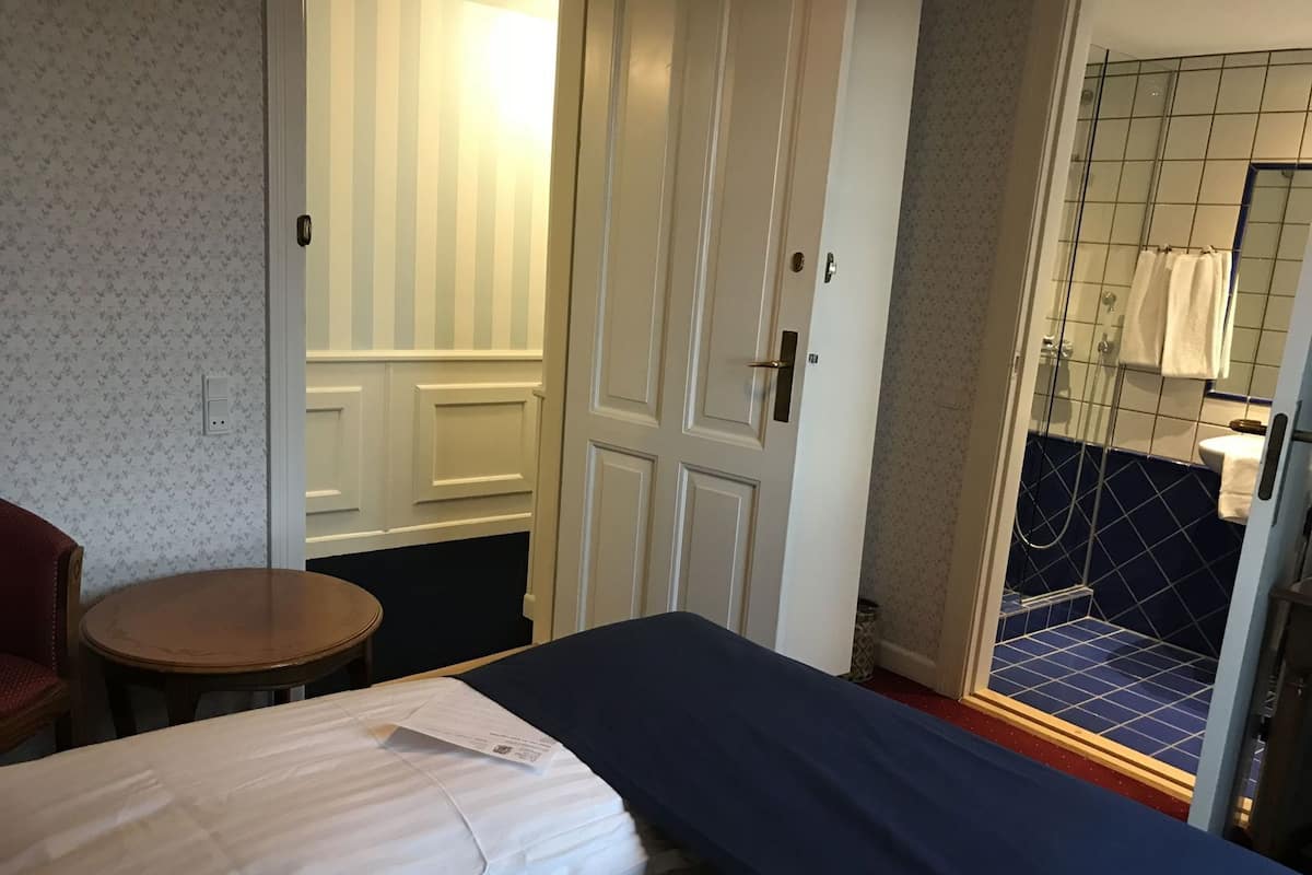 Habitación de hotel con dos camas, una mesita, una puerta y zona de ducha.