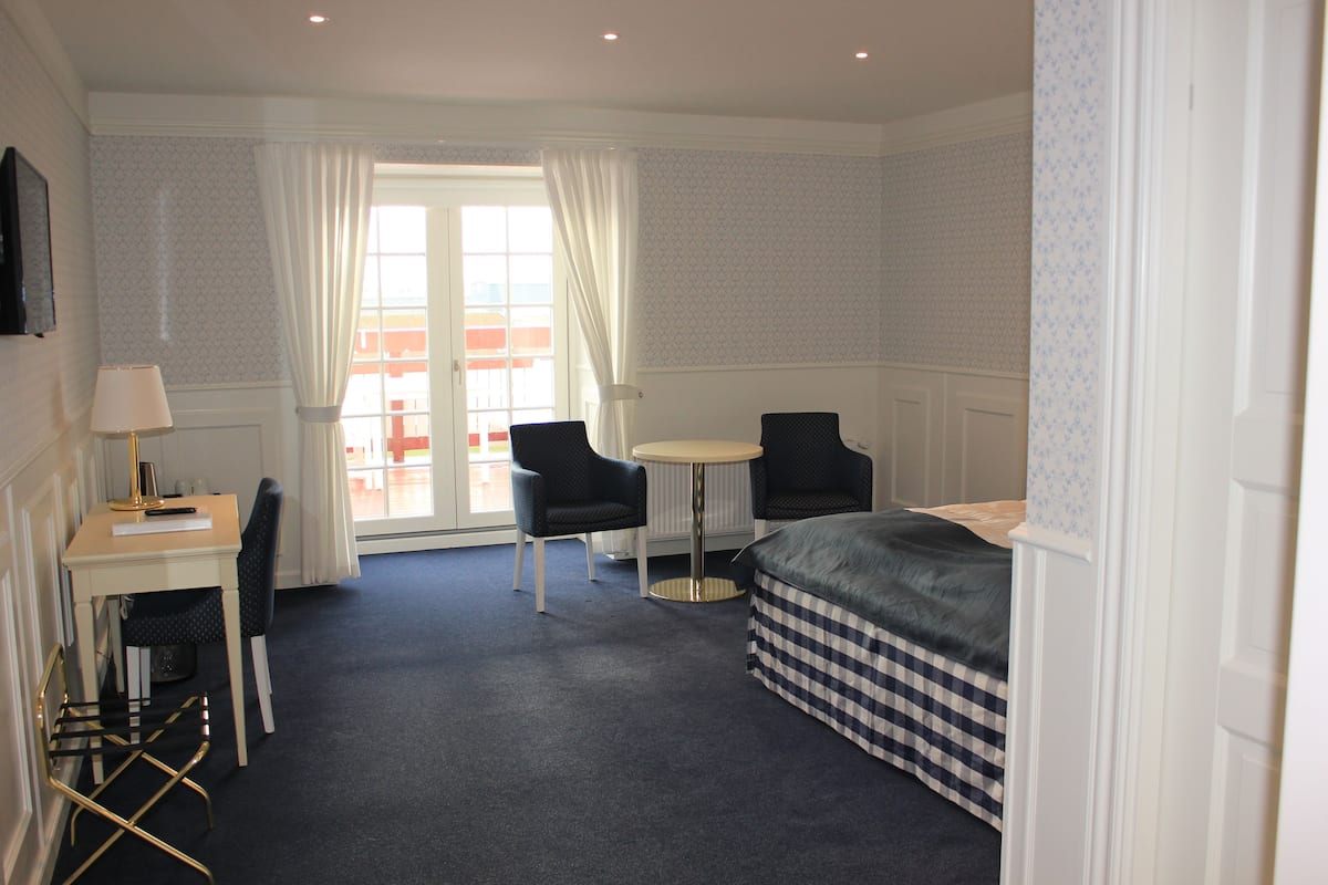 Habitación de hotel con cama, escritorio con silla, una mesita y ventana con cortinas.