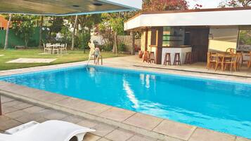 Ein Schwimmbecken mit Liegestühlen, einer überdachten Liegefläche und einer Bar.