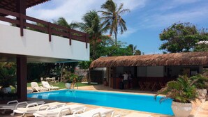 A swimming pool with lounge chairs, a bar area, and a thatched-roof structure. - Duro Beach Garden Hotel (Caucaia)