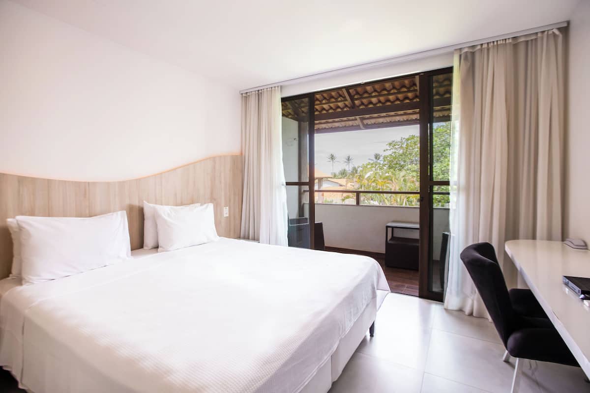 Ein Hotelzimmer mit einem großen Bett, einem Schreibtisch und einem Balkon mit Vorhängen.