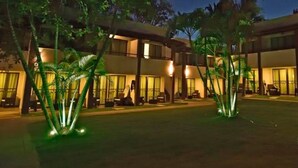 A hotel courtyard at night with illuminated palm trees and a building with multiple balconies. - Duro Beach Garden Hotel (Caucaia)