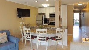 A modern kitchen with white cabinets, a built-in oven, and a stainless steel refrigerator. There is a dining area with white chairs and a blue sofa. - Updated Spectacular Kitchen Great Ocean Views Bikes & Beach Gear included (Hilton Head Island)