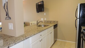A kitchen with granite countertops, white cabinets, a stainless steel sink, a black refrigerator, and a mounted television. - Updated Spectacular Kitchen Great Ocean Views Bikes & Beach Gear included (Hilton Head Island)