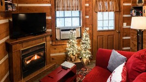 A log cabin interior with a fireplace, a television, a red couch, and a Christmas tree.