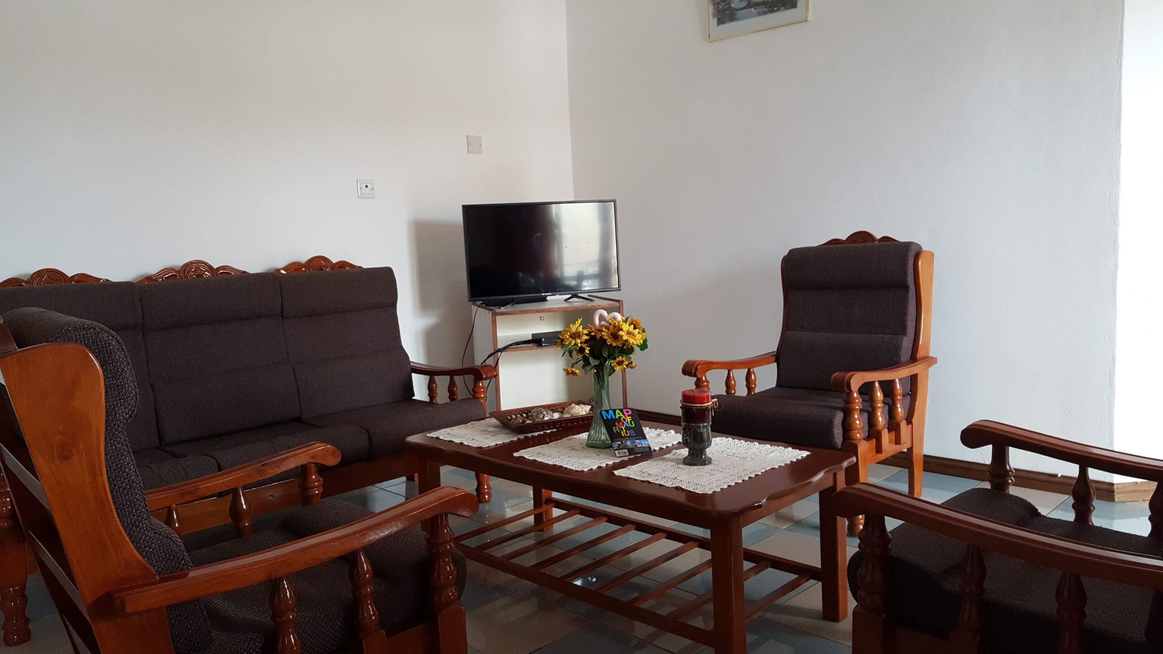 A living room with a sofa, two armchairs, a coffee table, a TV, and a vase with flowers.