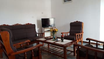 A living room with a sofa, two armchairs, a coffee table, a TV, and a vase with flowers.
