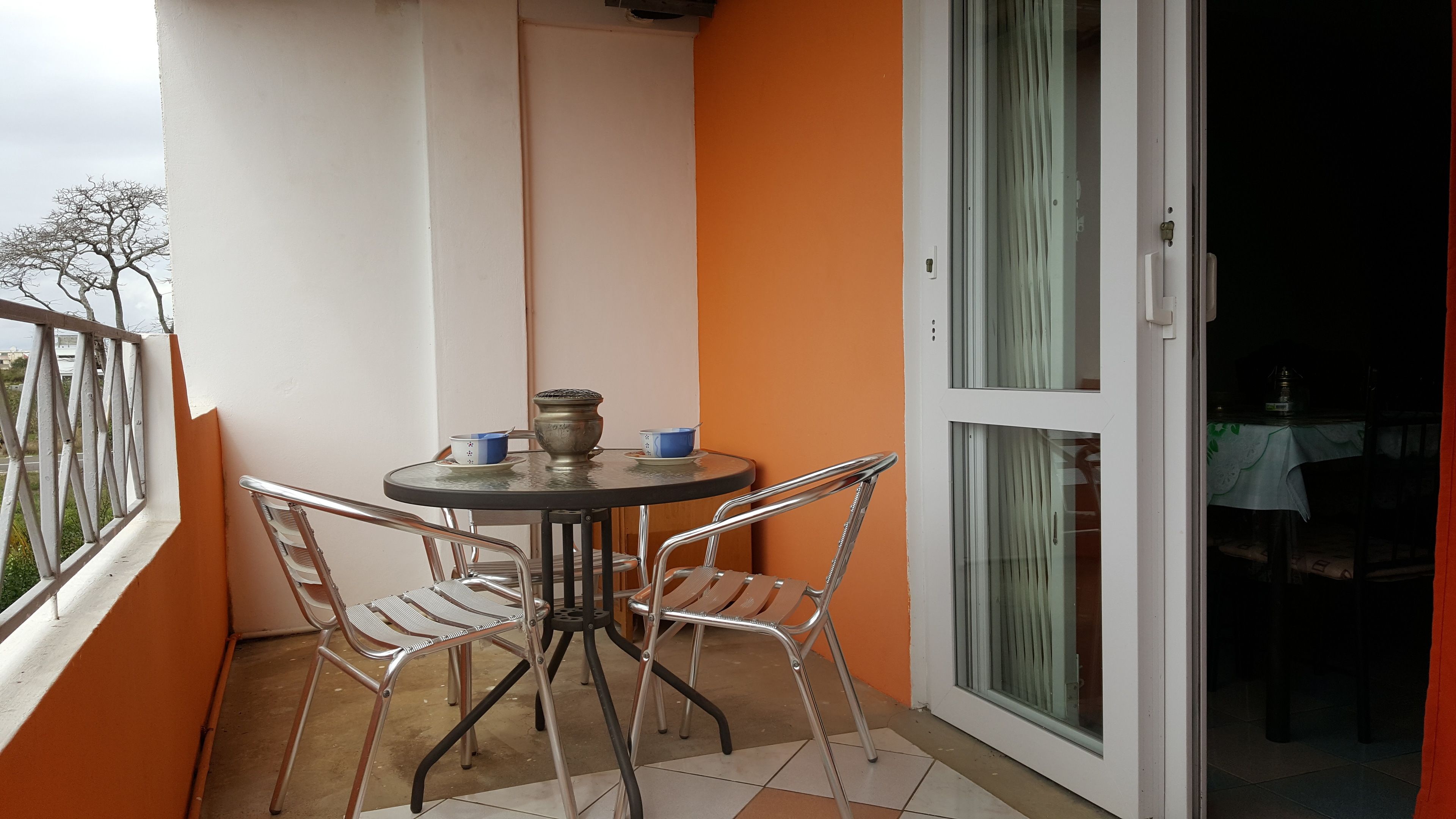 A small balcony with a round table and two chairs, a door with glass panels, and a view of the outdoors.