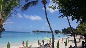 A beach with clear turquoise water, palm trees, and beach umbrellas. - The Impala Mauritius Holiday Rentals (Mont Choisy)
