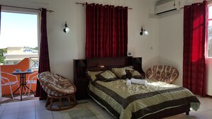 A bedroom with a bed, two chairs, a small table, and a window with curtains. - The Impala Mauritius Holiday Rentals (Mont Choisy)