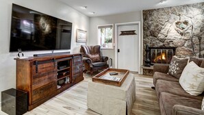 Un salon doté d’un grand téléviseur à écran plat, d’une cheminée en pierre, d’un canapé confortable et d’un meuble de rangement en bois pour les appareils multimédias.
