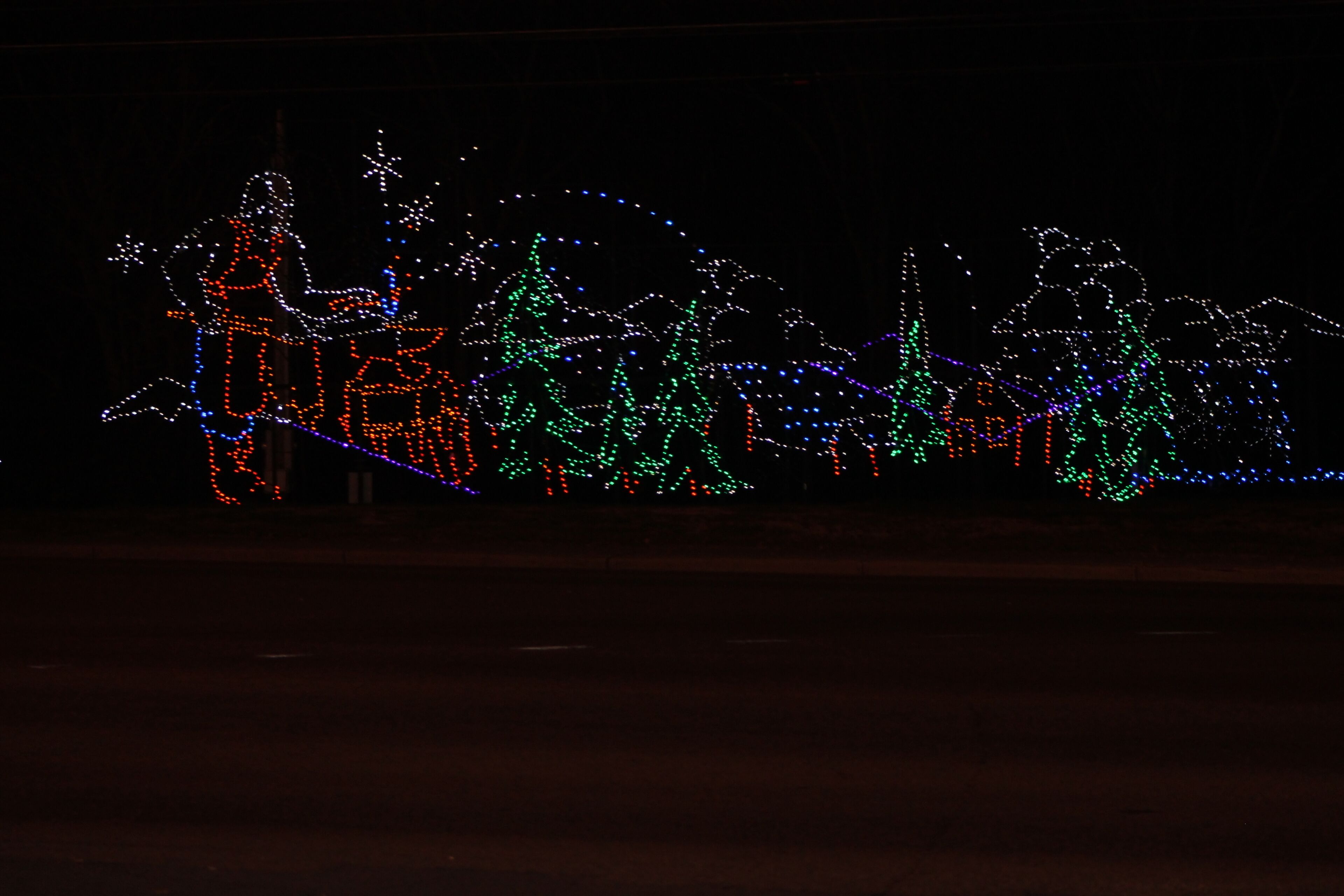 A dark scene with illuminated Christmas decorations, including figures and trees.