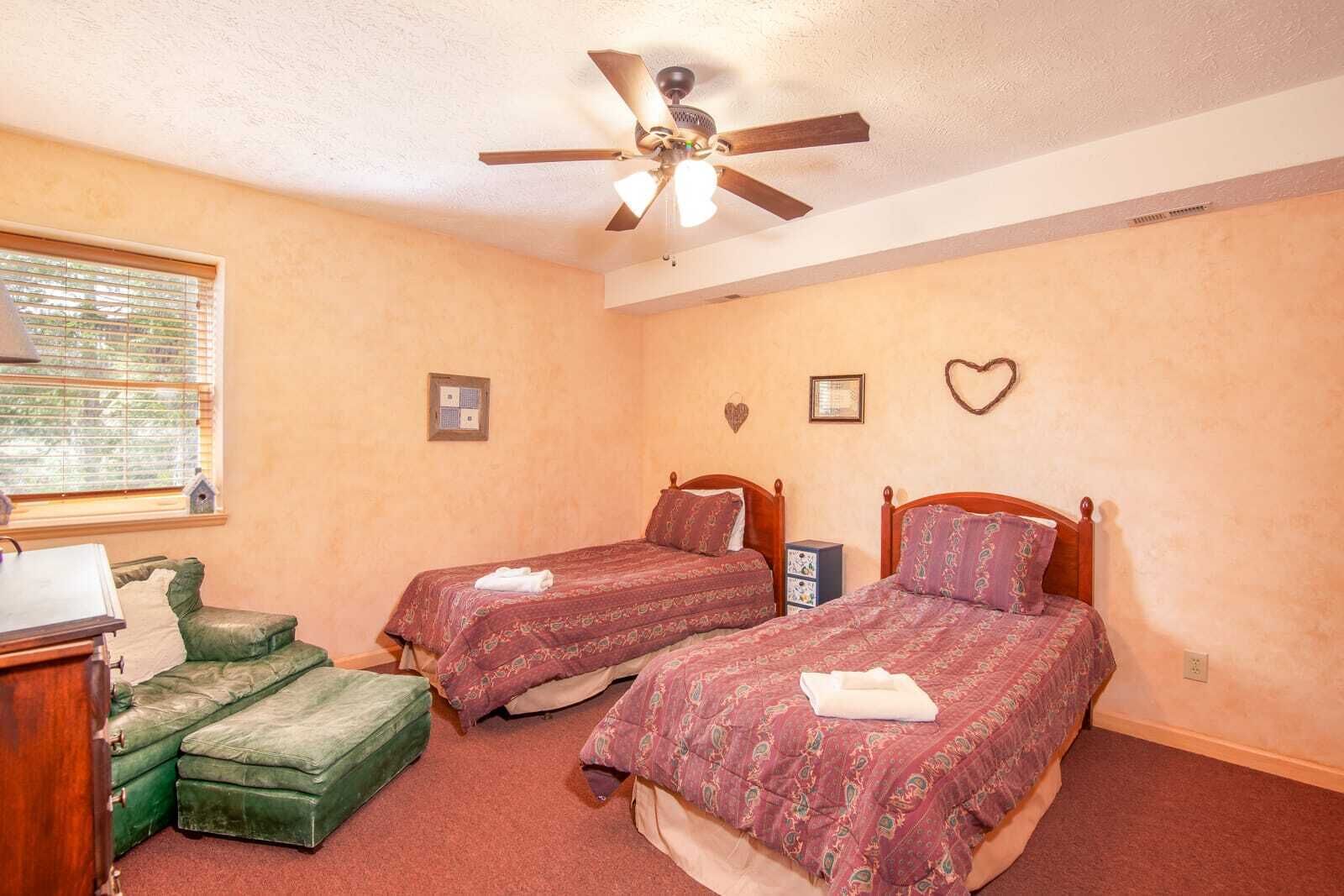 Ein Schlafzimmer mit zwei Betten, einem Deckenventilator, einem Fenster mit Jalousien und einer grünen Bank.