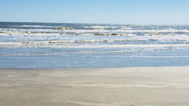 Una playa con olas acercándose a la orilla bajo un cielo despejado.