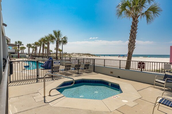 A pool area with a hot tub, lounge chairs, and a view of the beach.