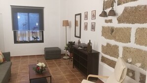 Ett vardagsrum med en soffa, ett soffbord med blommor, en tv, en lampa, ett litet bord med en vas och en dekorativ vägg.