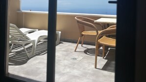 En balkong med utsikt över havet, inredd med flätade stolar och ett bord.