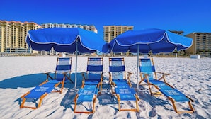 Beach chairs with blue canopies and a 'DO NOT SIT LEG REST' sign, set against a backdrop of high-rise buildings.