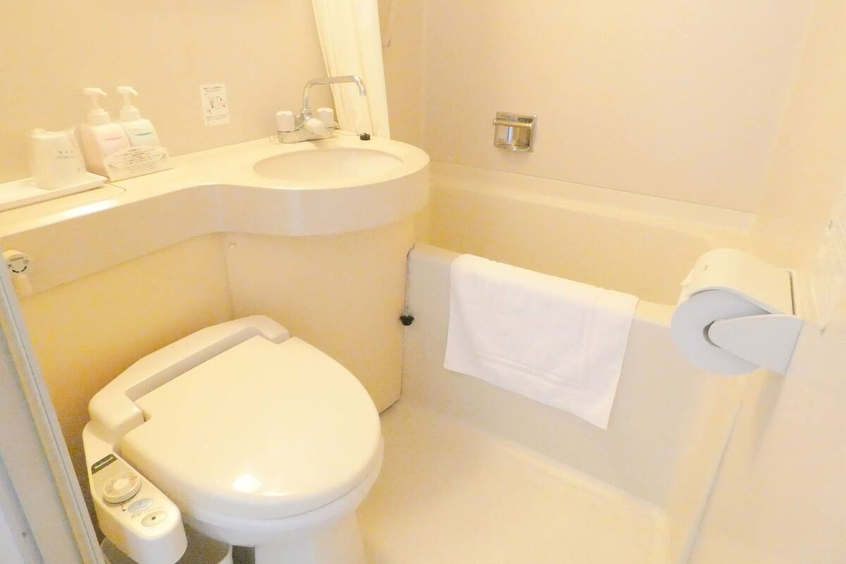 Une petite salle de bain blanche, avec des toilettes, un lavabo et une serviette accrochée au mur.