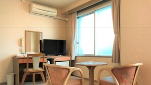 Ein Hotelzimmer mit Schreibtisch, Fernseher, zwei Stühlen, einem kleinen Tisch, einem Spiegel und einem fenster mit Vorhängen.
