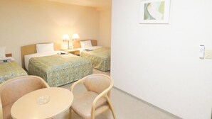 Ein Hotelzimmer mit zwei Betten, einem kleinen Tisch, zwei Stühlen und einer Wandleuchte.