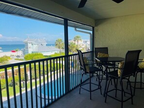 A balcony with a view of the ocean, a pool, and a building with a white roof. - Sunset Beach 202 2 Bedroom Condo by RedAwning (Holmes Beach)