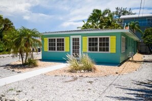 A small, single-story building with a flat roof, a front door, and a window with a shutter. - 3706 Gulf Dr 2 Bedroom Home by RedAwning (Holmes Beach)
