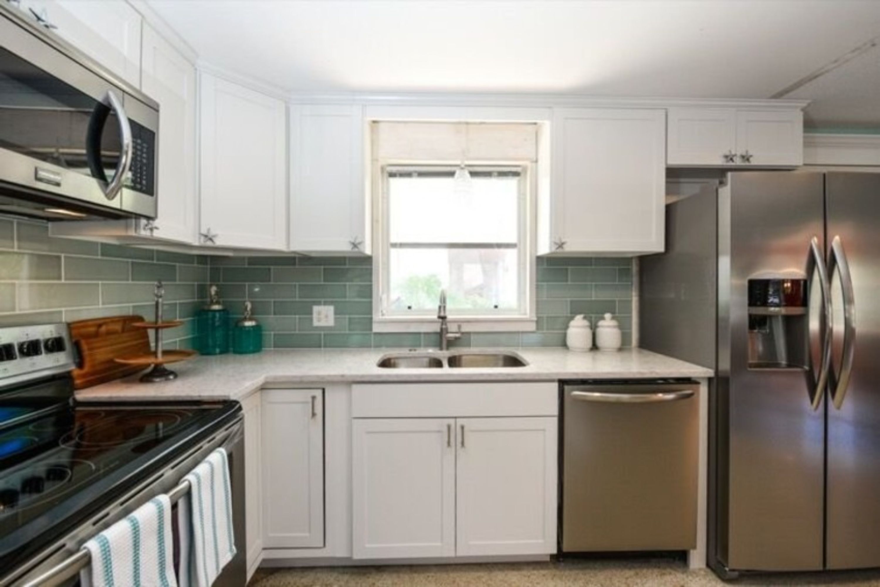 A modern kitchen with white cabinets, a stainless steel refrigerator, a microwave, and a dishwasher.