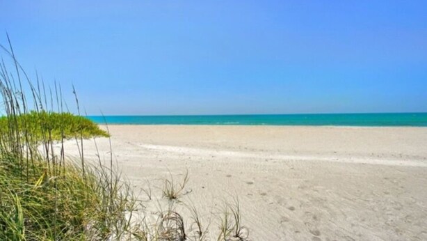 A beach with clear blue water and sandy shore. - 3706 Gulf Dr 2 Bedroom Home by RedAwning (Holmes Beach)