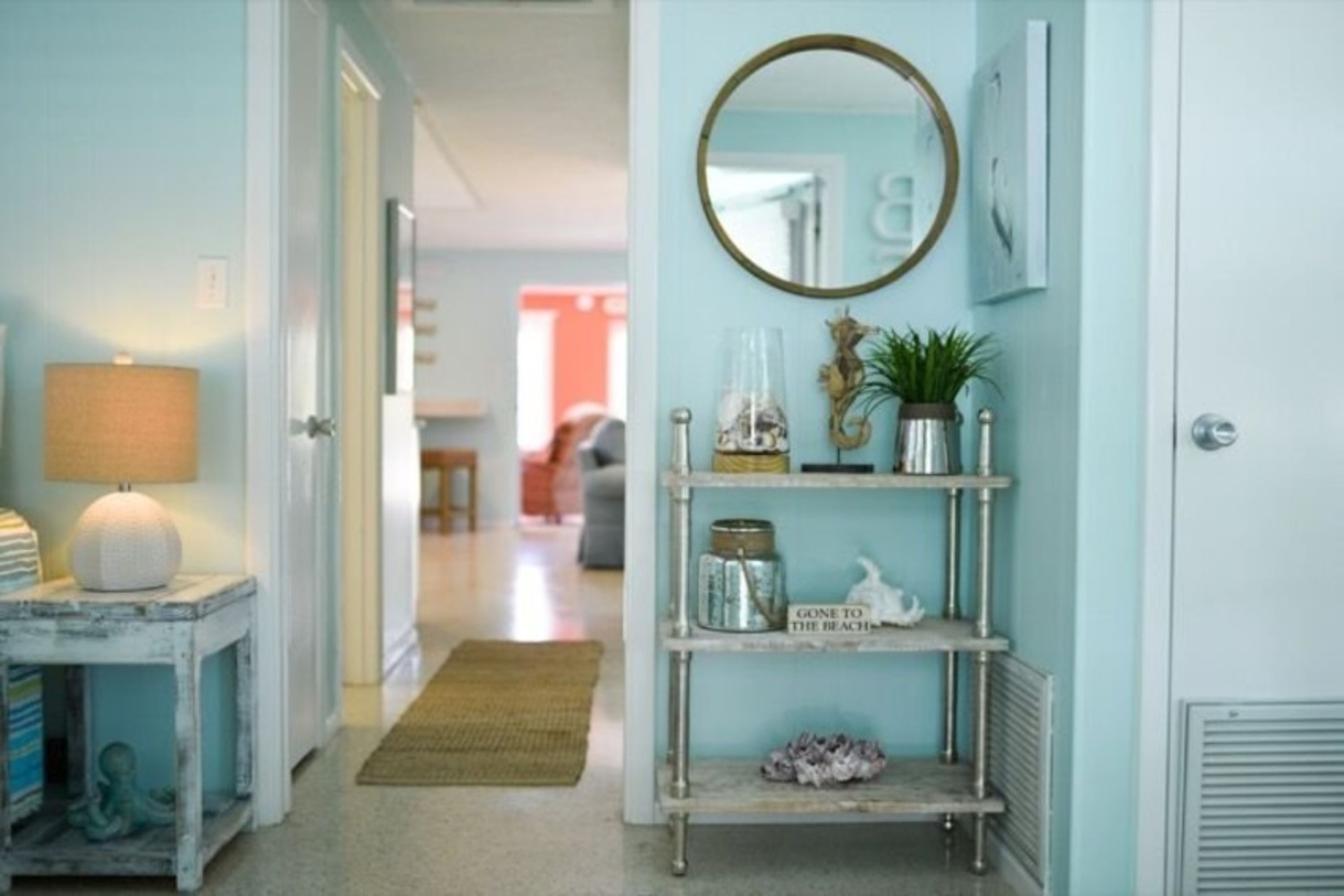 A hallway with a lamp, a shelf with decorative items, and a mirror on the wall.