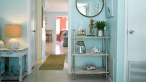 A hallway with a lamp, a shelf with decorative items, and a mirror on the wall. - 3706 Gulf Dr 2 Bedroom Home by RedAwning (Holmes Beach)