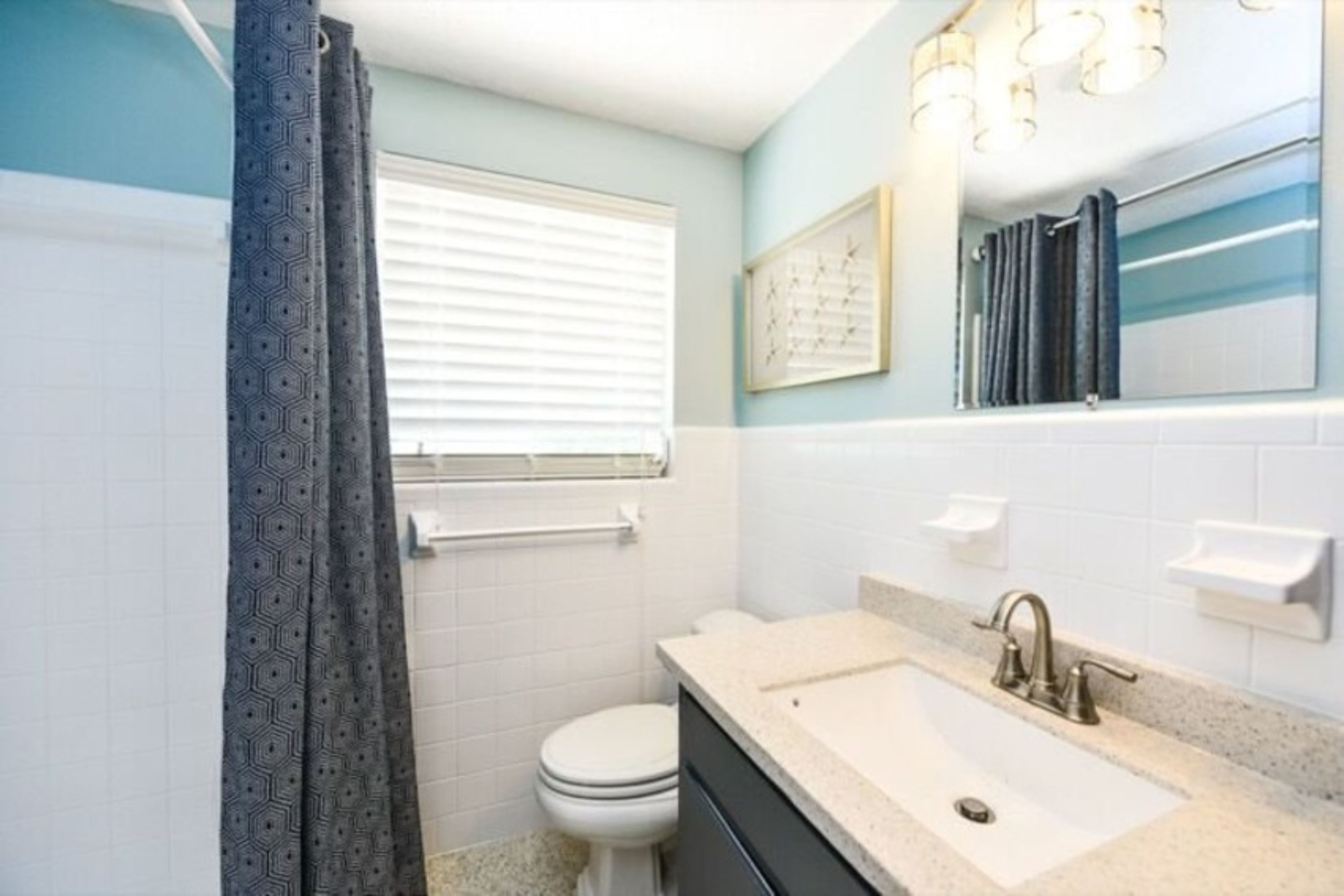 A bathroom with a white toilet, a sink with a beige countertop, and a window with blinds.