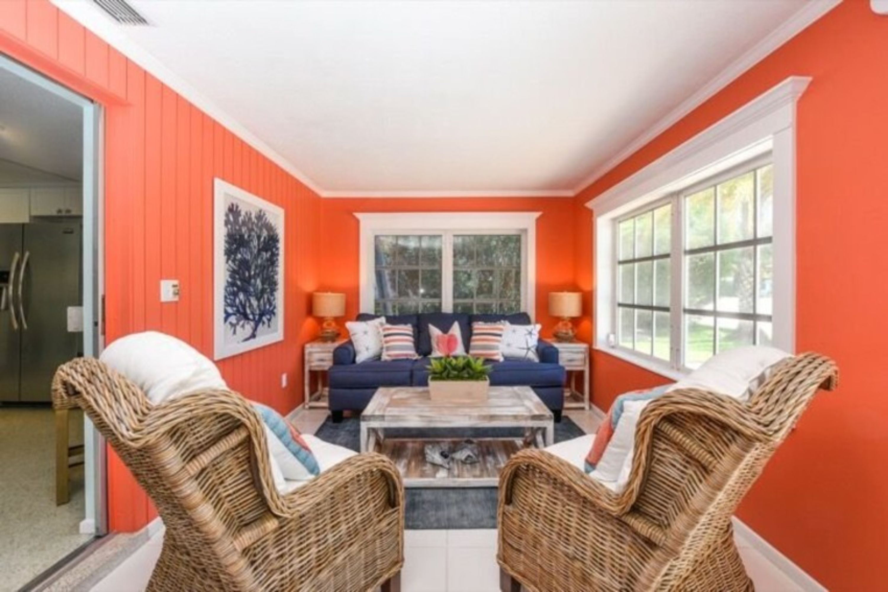 A living room with a blue sofa set, wicker chairs, a coffee table, and a large window.