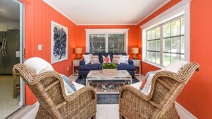 A living room with a blue sofa set, wicker chairs, a coffee table, and a large window. - 3706 Gulf Dr 2 Bedroom Home by RedAwning (Holmes Beach)