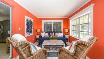 A living room with a blue sofa set, wicker chairs, a coffee table, and a large window.