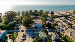 An aerial view of a coastal area with a beach, parking lots, and a building surrounded by trees. - 3902 Gulf Dr 1 1 Bedroom Apts by RedAwning (Holmes Beach)