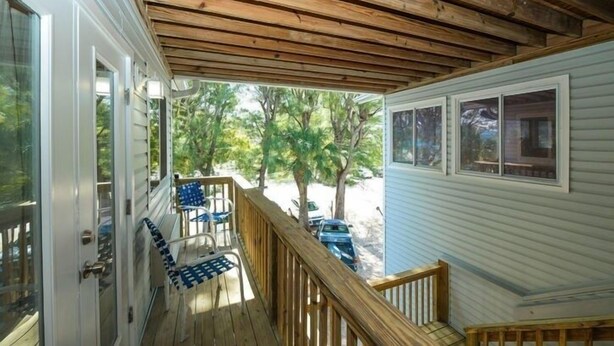 A covered porch with wooden beams, a white door, and a view of a tree-lined street. - 3902 Gulf Dr 1 1 Bedroom Apts by RedAwning (Holmes Beach)