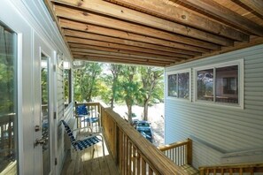 A covered porch with wooden beams, a white door, and a view of a tree-lined street. - 3902 Gulf Dr 1 1 Bedroom Apts by RedAwning (Holmes Beach)