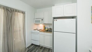 A compact kitchen with white cabinets, a microwave, a stove, and a refrigerator. - 3902 Gulf Dr 1 1 Bedroom Apts by RedAwning (Holmes Beach)