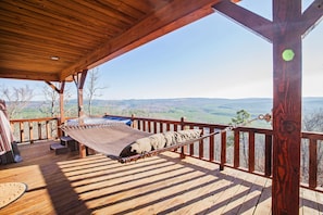 Relax in a hammock on this outdoor deck overlooking the scenic landscape with distant hills and trees.