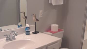 A bathroom with a white sink, mirror, and toilet. There are two framed pictures on the wall, a towel rack with a white towel, and a roll of toilet paper on the toilet.