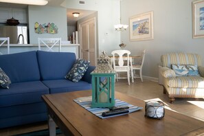 Un salon avec un canapé bleu, un fauteuil à motifs, une table basse en bois et une lanterne turquoise.