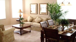 A living room with a sofa, armchairs, a coffee table, a dining table set for two, and a large plant. - 506 BONVILLE (Davenport)