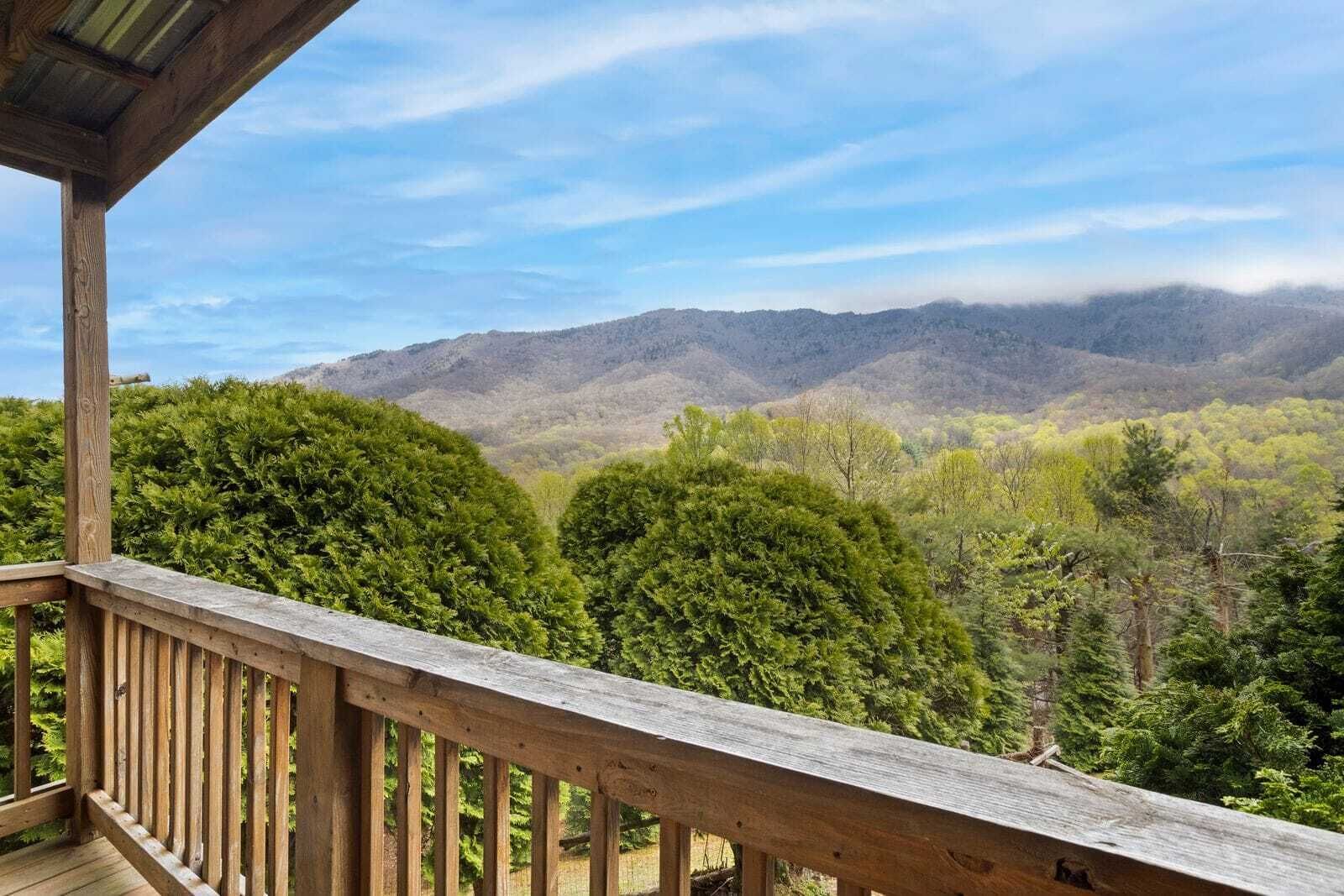 A wooden deck overlooking a forested valley with distant mountains.