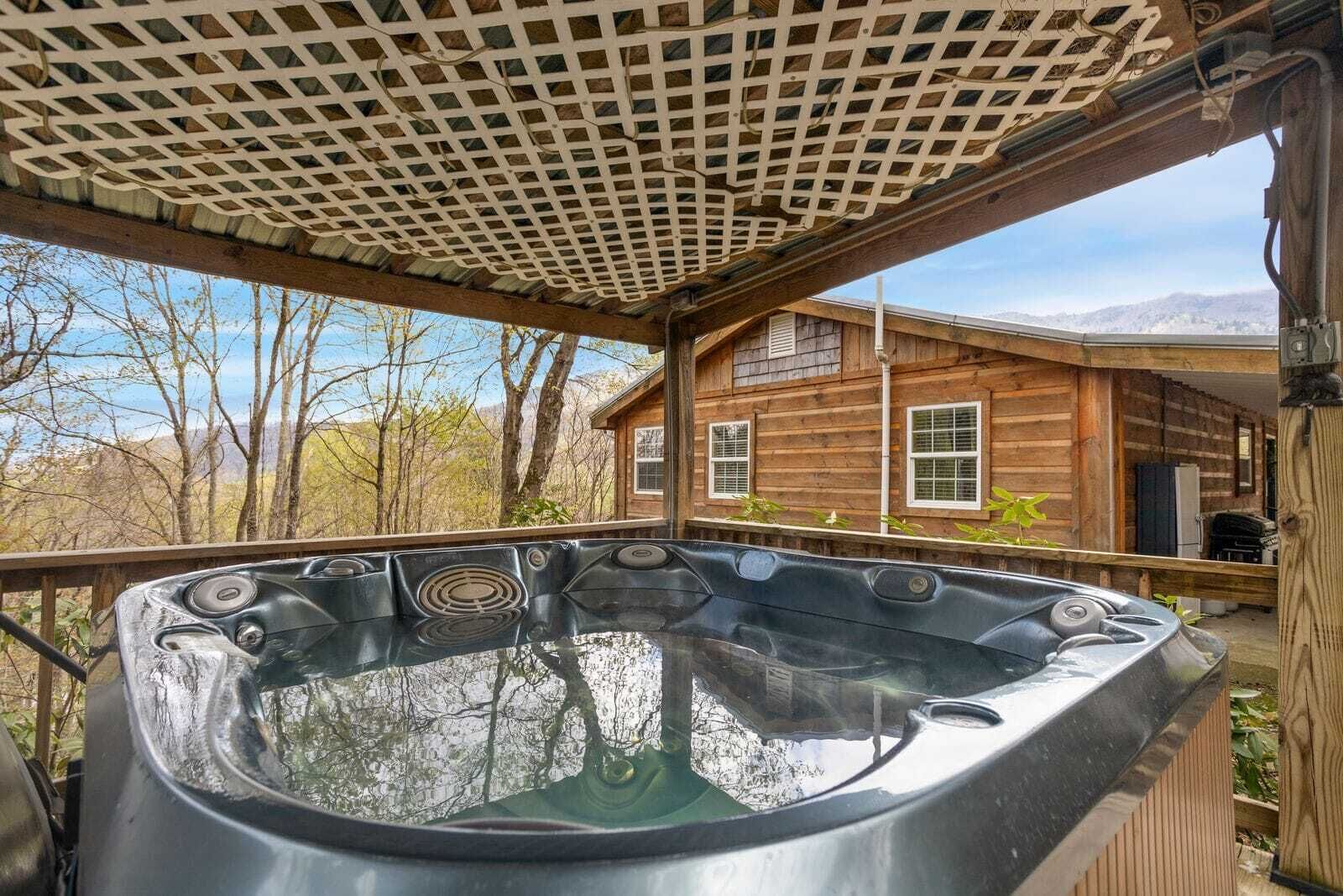 A hot tub under a wooden pergola with a view of a wooden cabin.