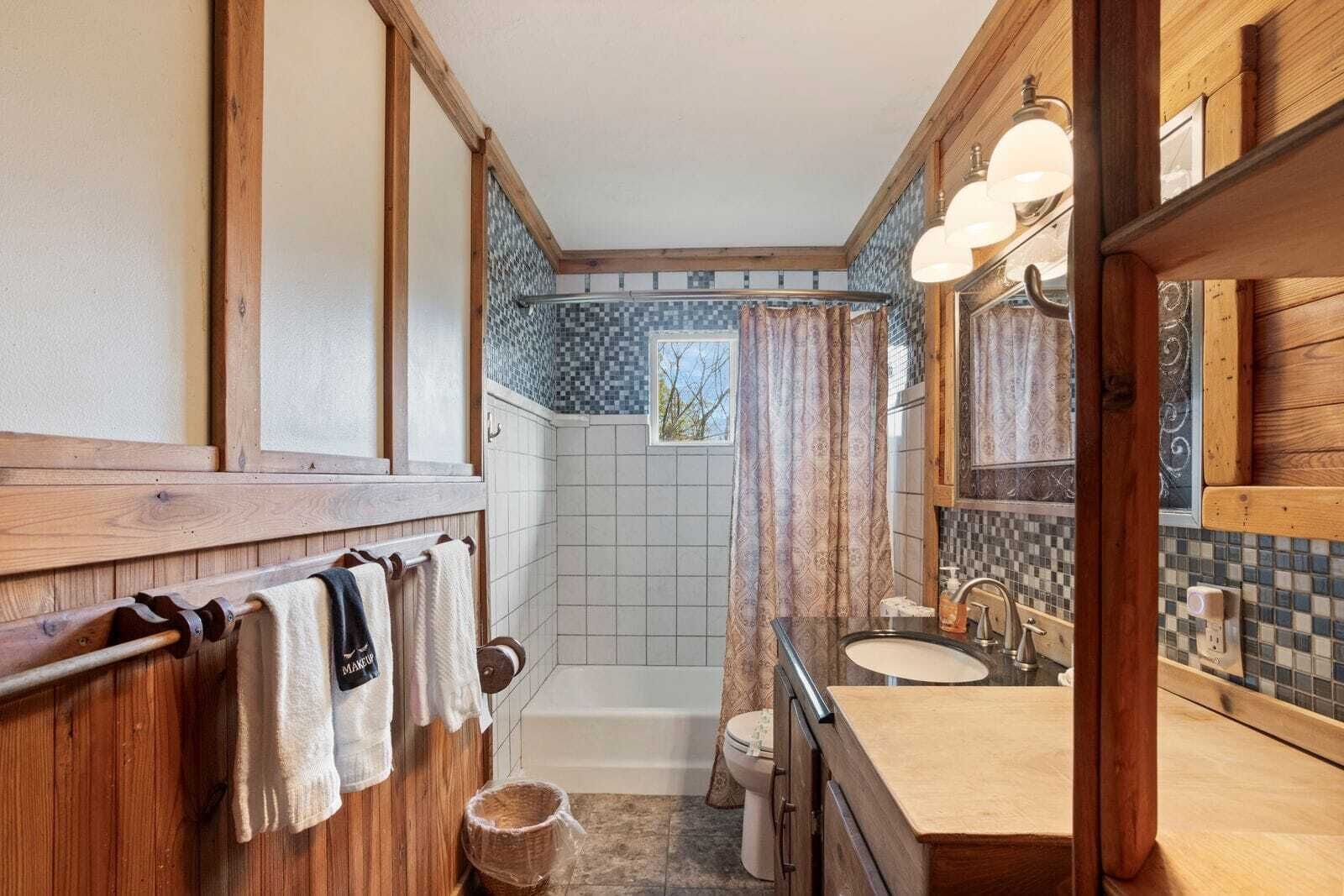 Une salle de bain avec des meubles en bois, une baignoire, des toilettes et un lavabo avec un miroir.